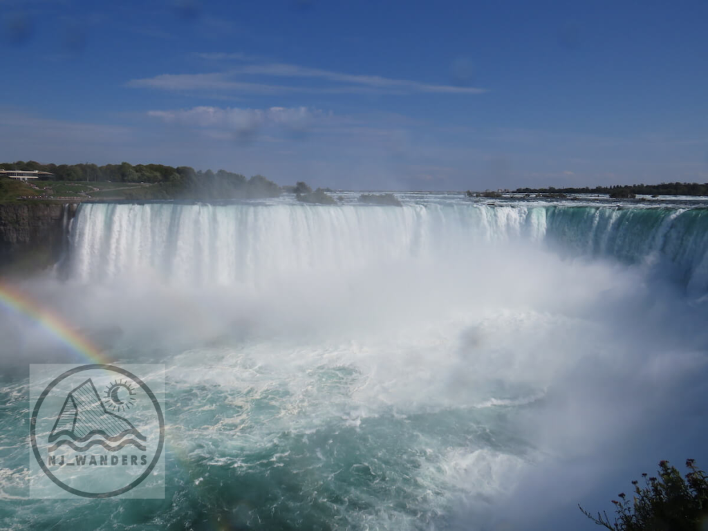 The horseshoe shape of Niagara Falls rushing over the drop with a rainbow in the corner