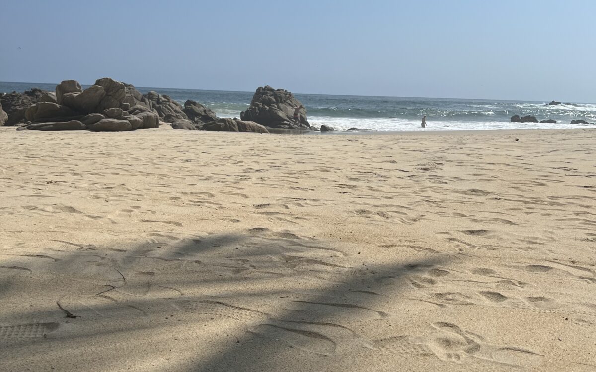 a sandy beach with rocks as the sand meets the sea