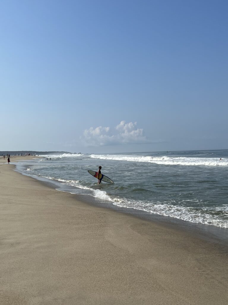 Golden sand and the sea with a surfer standing watching the waves